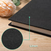 A close-up view of a black magnetic scrapbook album with a linen texture, showing the spine and a detail circle.