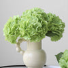 A vase holds a bouquet of light green artificial hydrangea stems.