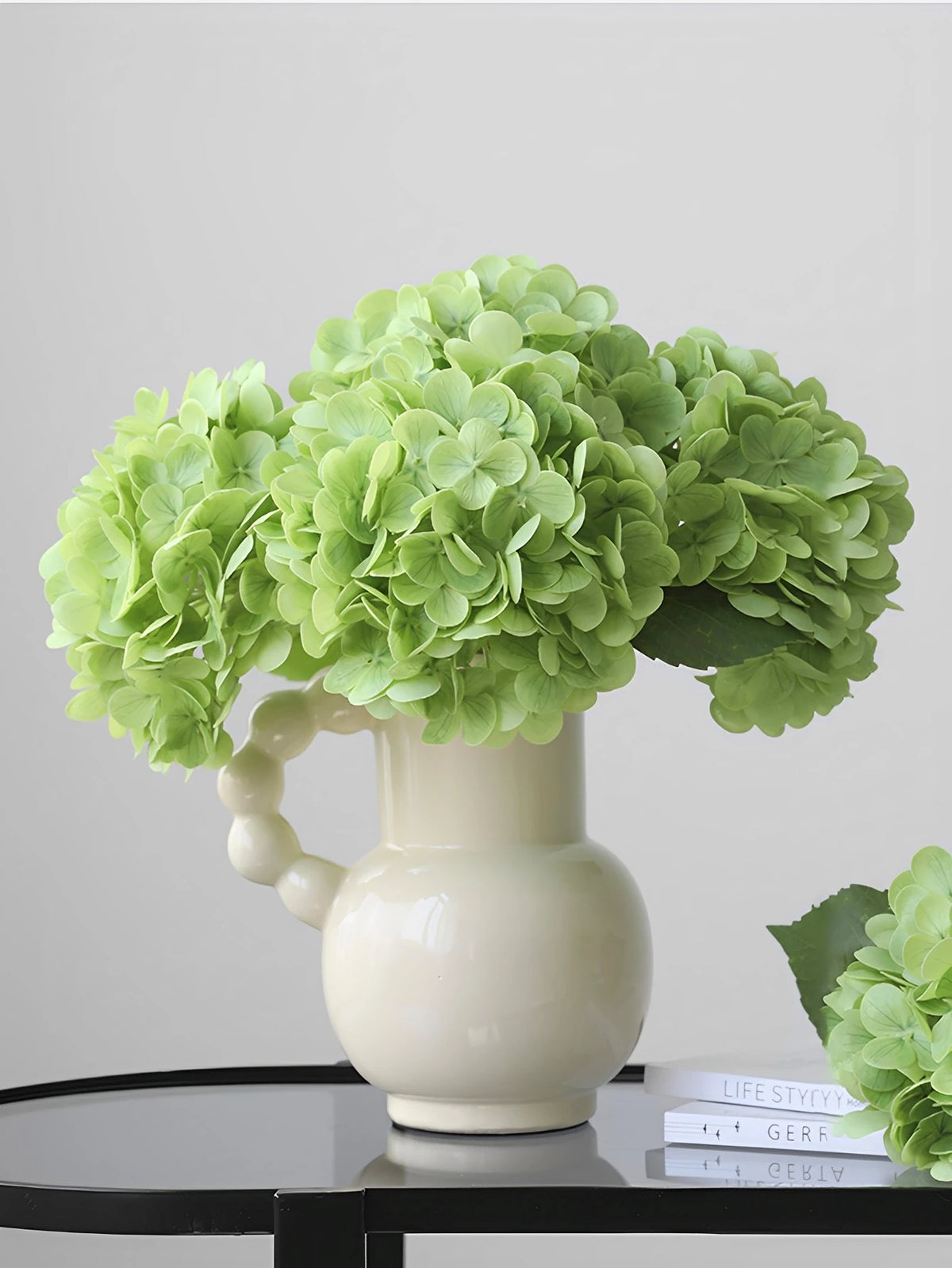A vase holds a bouquet of light green artificial hydrangea stems.