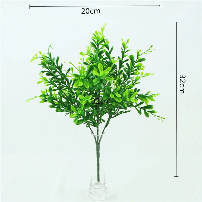 A vibrant green artificial fern with leaf sprigs displayed in a glass vase.