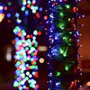 Close-up of bright, multicolored LED string lights wrapped around a green pole in a dark outdoor setting.