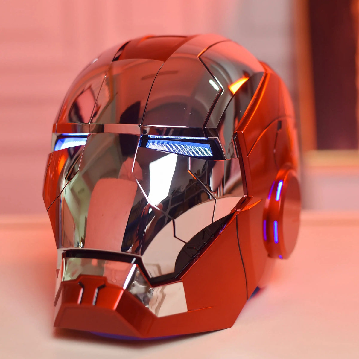 An Iron Man MK5 wearable helmet in metallic orange with blue LED lights, shown from the front.