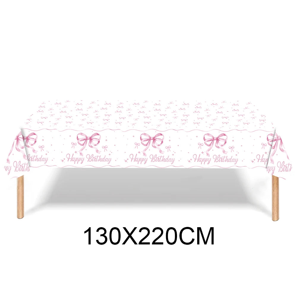 Pink bow disposable party tableware set with birthday decorations displayed on a table.