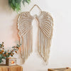 Handwoven angel wing macrame wall hanging in beige natural fiber suspended on a white wall.