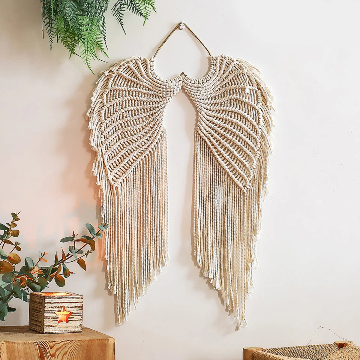 Handwoven angel wing macrame wall hanging in beige natural fiber suspended on a white wall.