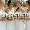 Five brides in white dresses holding bouquets of white roses and greenery
