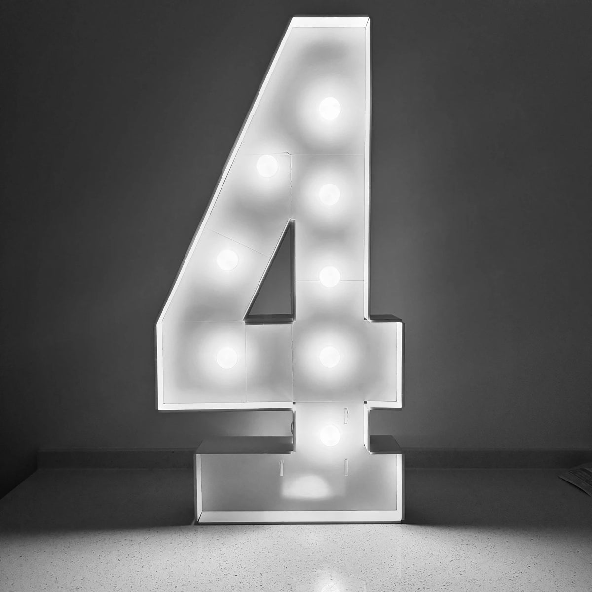 A glowing white marquee number sign shaped like the numeral 4 displayed on a gray wall.