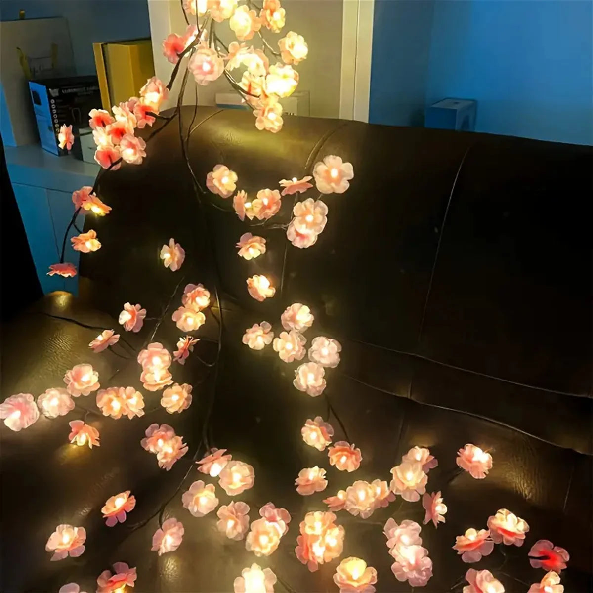 LED rattan string lights with pink and orange flowers decorating a dark leather sofa.