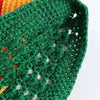 A close-up of a handmade crochet beanie hat in dark green yarn with orange accents.