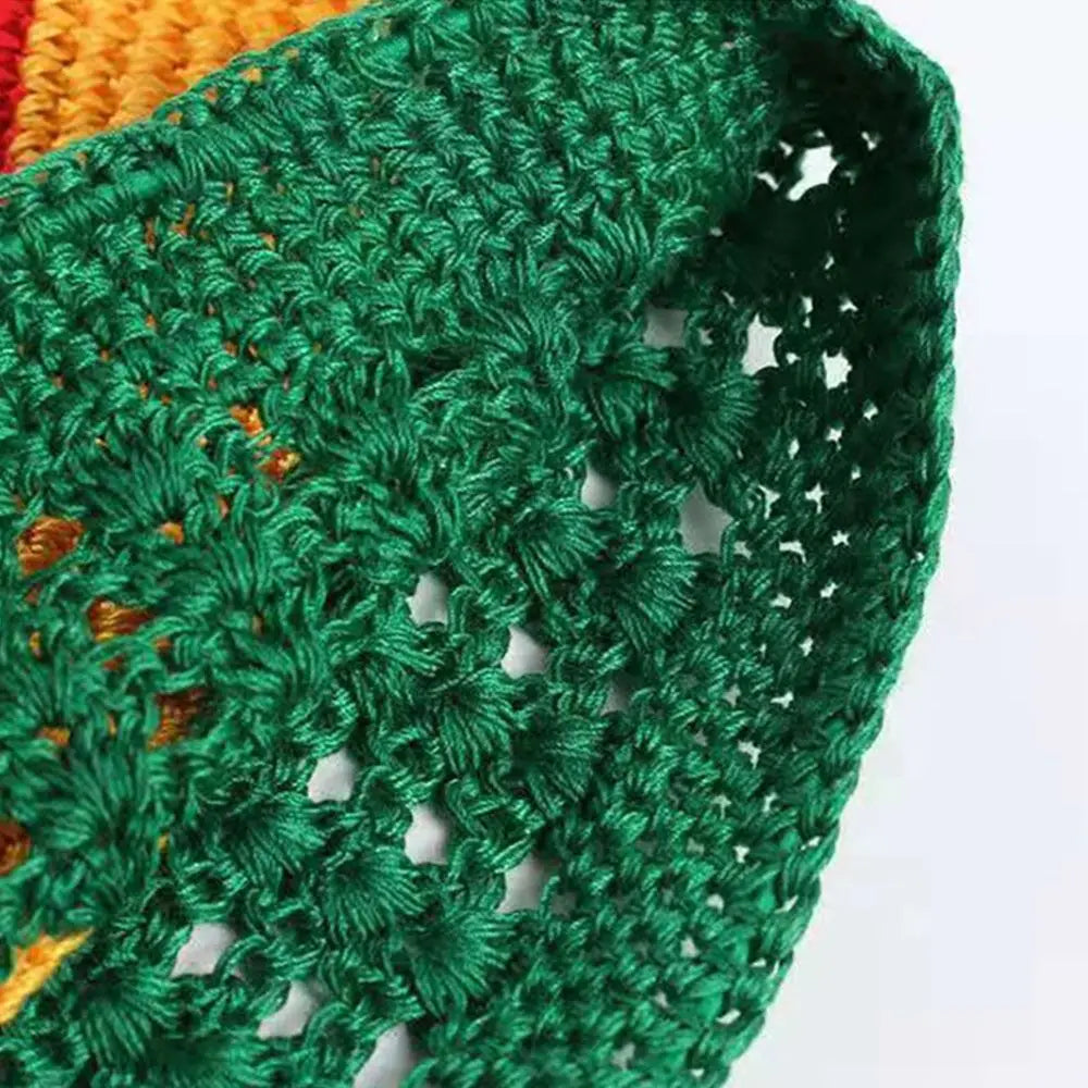 A close-up of a handmade crochet beanie hat in dark green yarn with orange accents.
