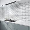 A modern kitchen featuring white subway tile backsplash, gray cabinets, and a stainless steel range hood.