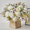 A bouquet of white and cream artificial silk flowers featuring roses, daisies, and filler greenery in a gold textured box.