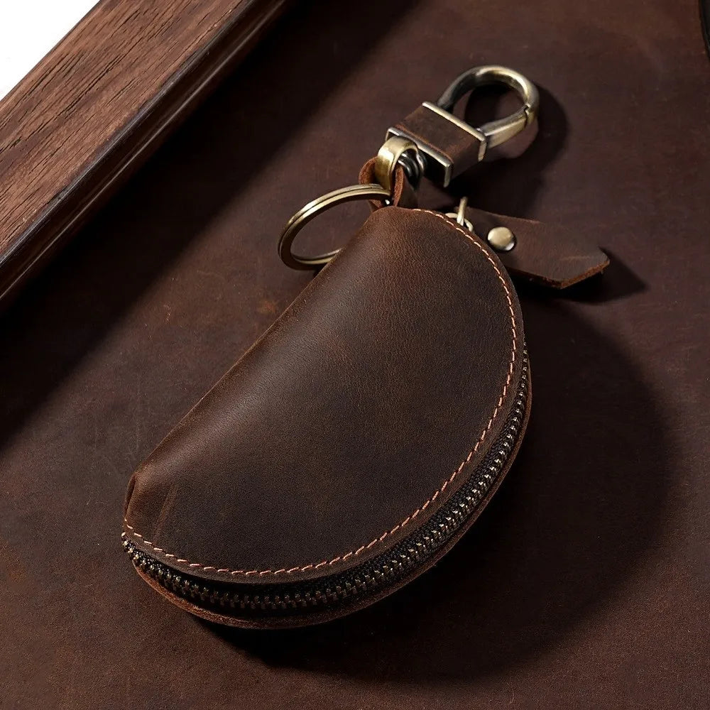 A dark brown leather key pouch with a brass carabiner attached, resting on a dark wooden surface.