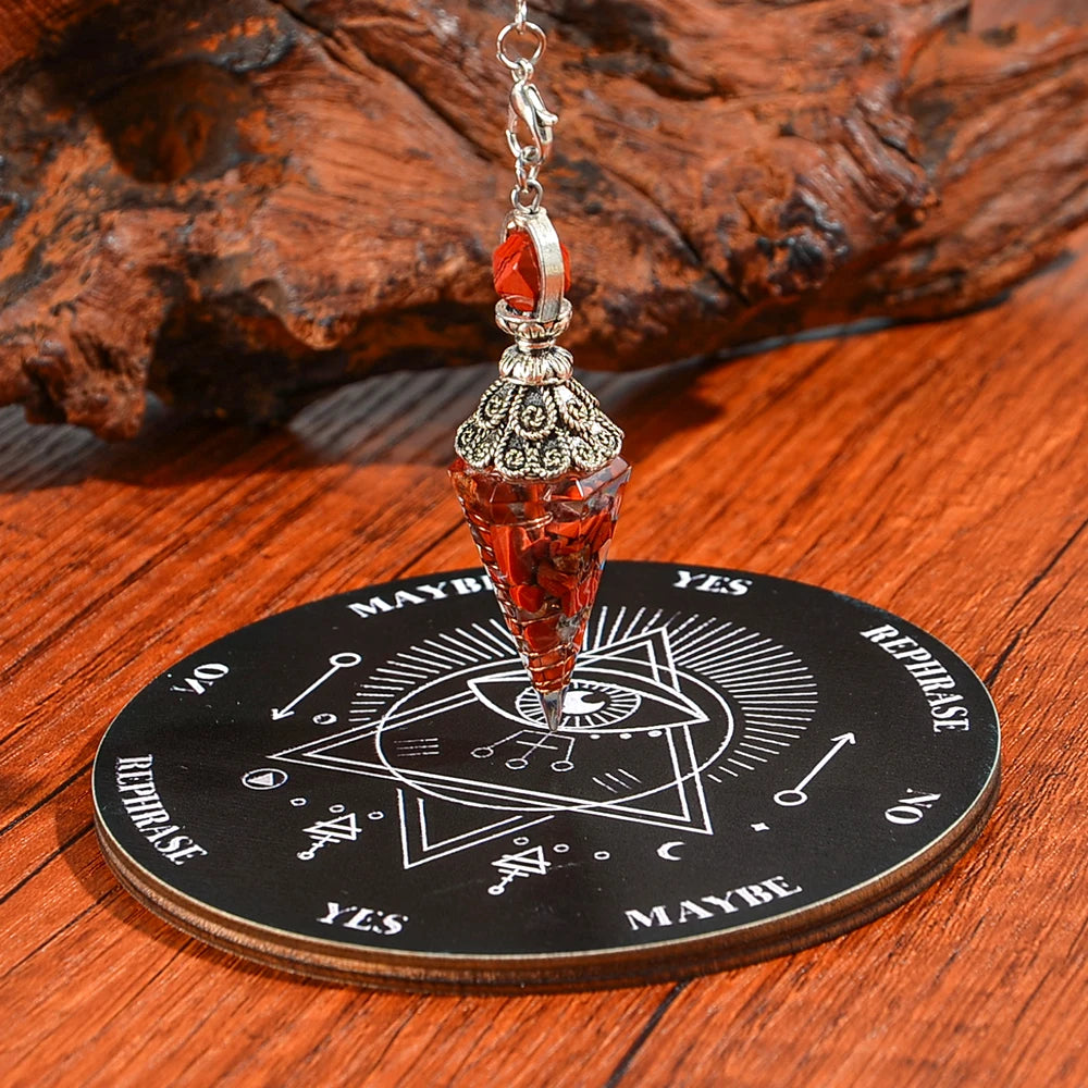 A crystal pendulum set featuring a red gemstone and silver findings displayed on a wooden divination board.