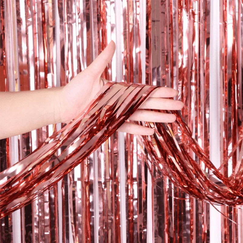 A hand is pulling metallic copper foil fringe curtain strands against a pink and silver background.