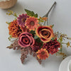 A bouquet of artificial silk flowers in shades of orange, pink, and mauve arranged on a white surface.