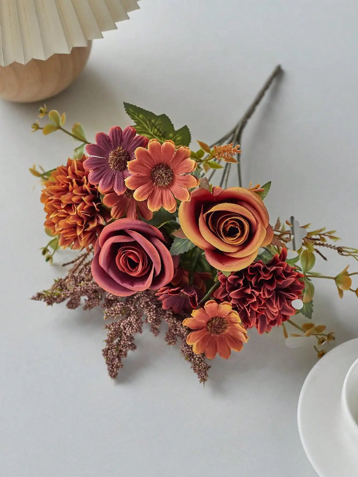 A bouquet of artificial silk flowers in shades of orange, pink, and mauve arranged on a white surface.