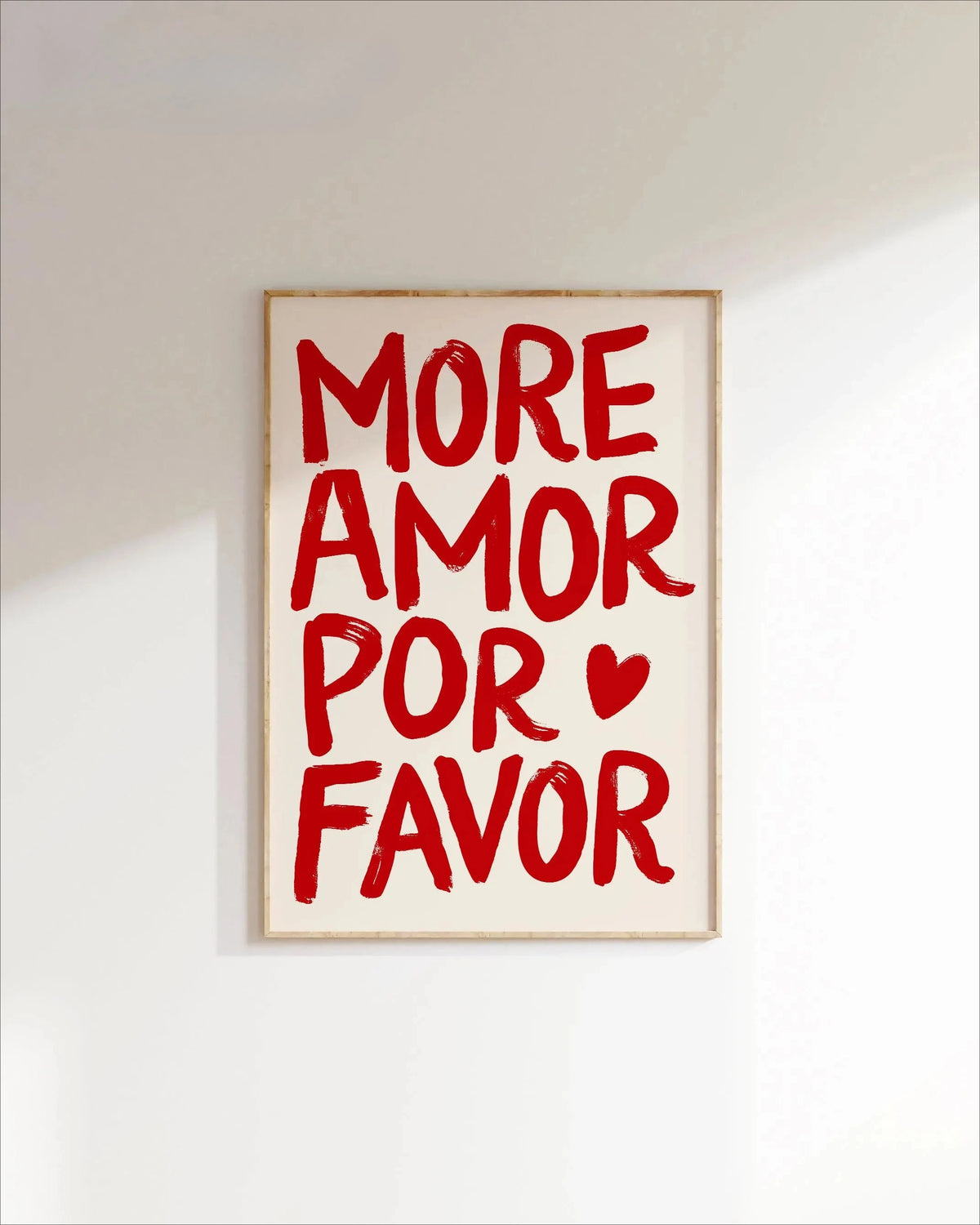 A framed canvas print with red text that reads MORE AMOR POR FAVOR on a white background.