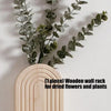 A wooden wall rack for dried flowers and plants made of eucalyptus branches mounted on a light wood panel.