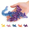 A hand holds a purple and blue 3D printed magic dragon ornament with various colored dragon shapes below.