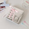 A silver leather photo album with a pink ribbon closure and a small white smile charm is displayed on a white surface.