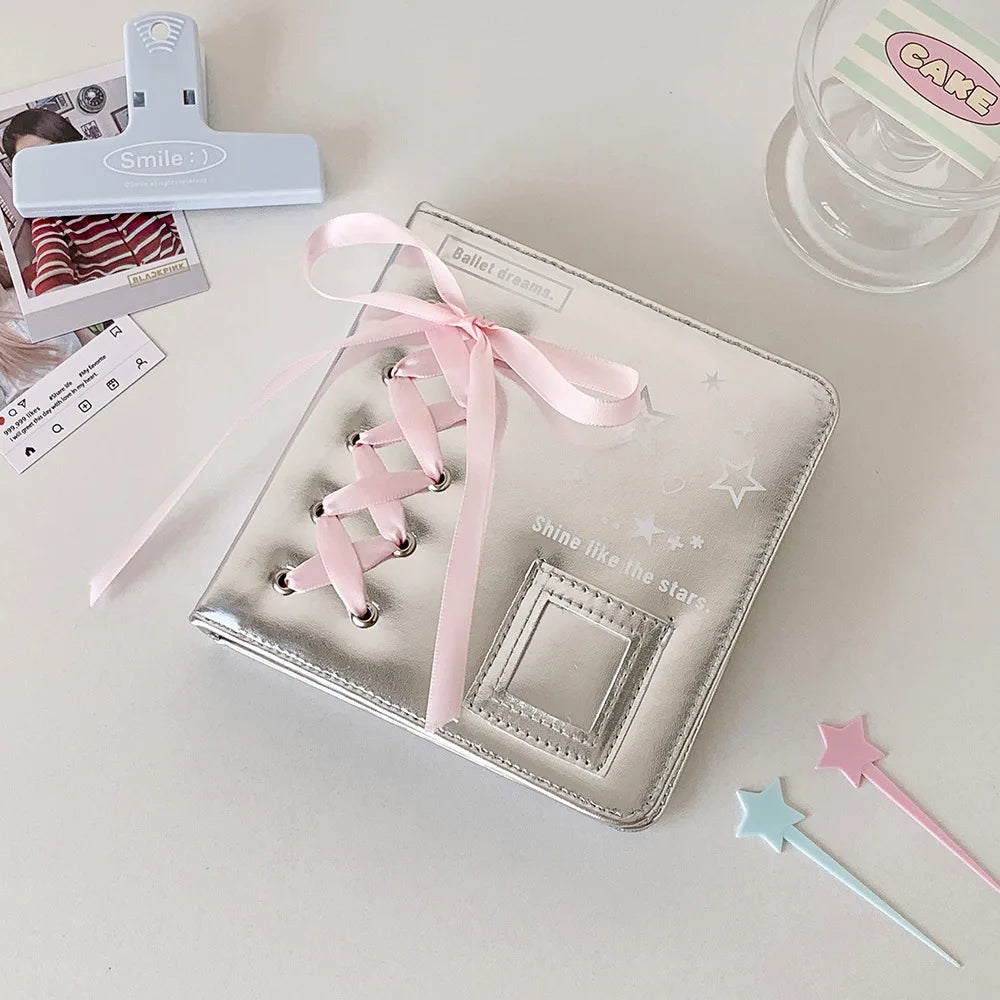 A silver leather photo album with a pink ribbon closure and a small white smile charm is displayed on a white surface.