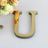 A gold letter U cutout for a mirror wall decal set, placed next to some flowers.