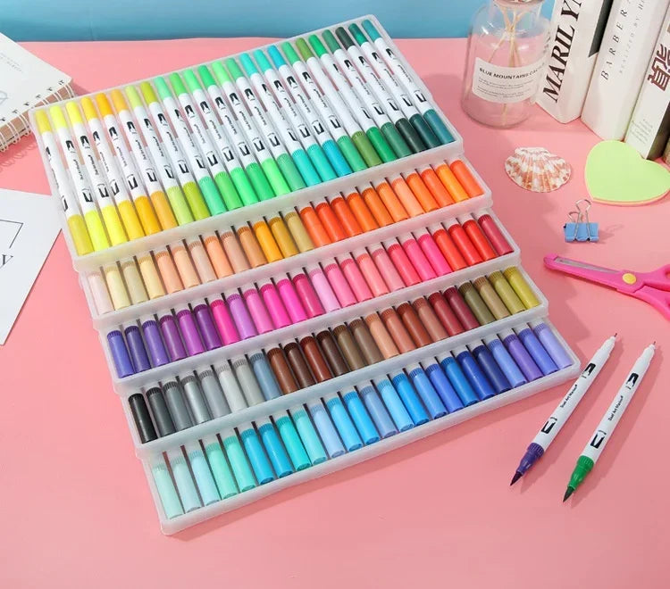 A colorful set of dual-ended watercolor art markers arranged in a plastic case on a pink surface.