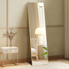 A full length arched wall mirror with a gold frame reflects a modern lamp and a chair in a light-colored room.