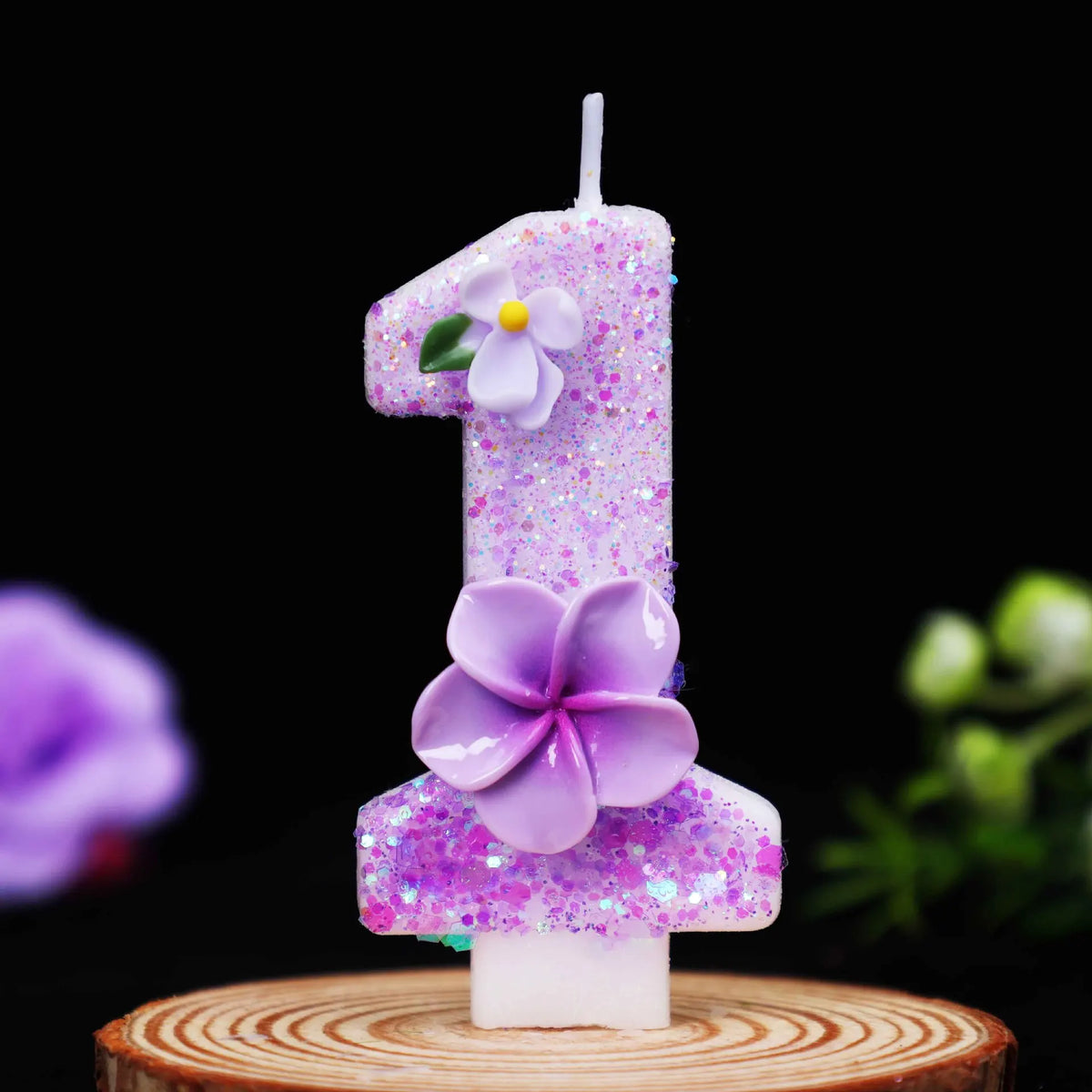 A glitter purple flower number candle shaped like the number one on a wooden surface.