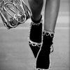 A close-up, black and white photograph of a person's legs wearing black high heels with sparkling embellishments.