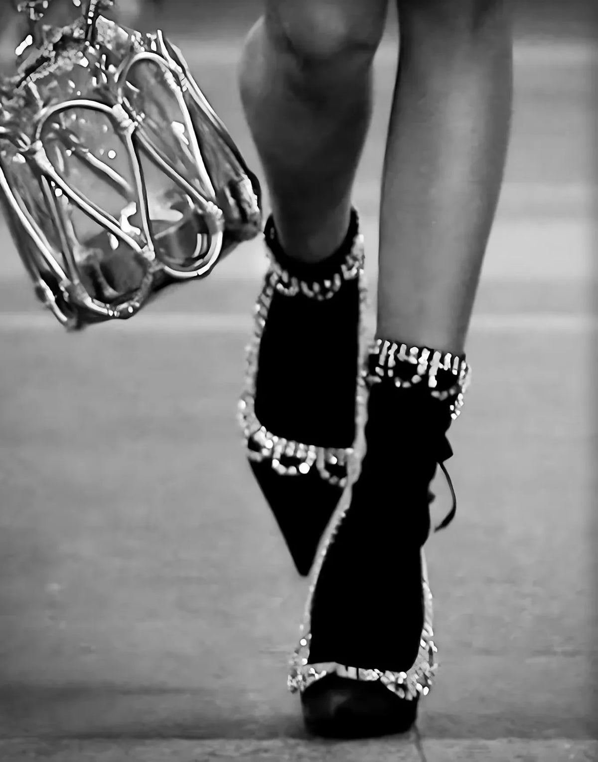 A close-up, black and white photograph of a person's legs wearing black high heels with sparkling embellishments.
