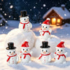 A collection of white and red resin snowman figurines resting on snow in a winter outdoor setting.