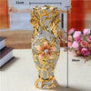 A tall, ornate gold-plated ceramic tabletop vase with floral accents and a textured silver body.
