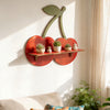 A wooden cherry-shaped wall shelf displaying small potted succulents and decorative figures on a white wall.