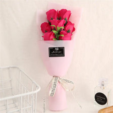 A pink vase holds a bouquet of vibrant pink roses with a black tag and twine bow.