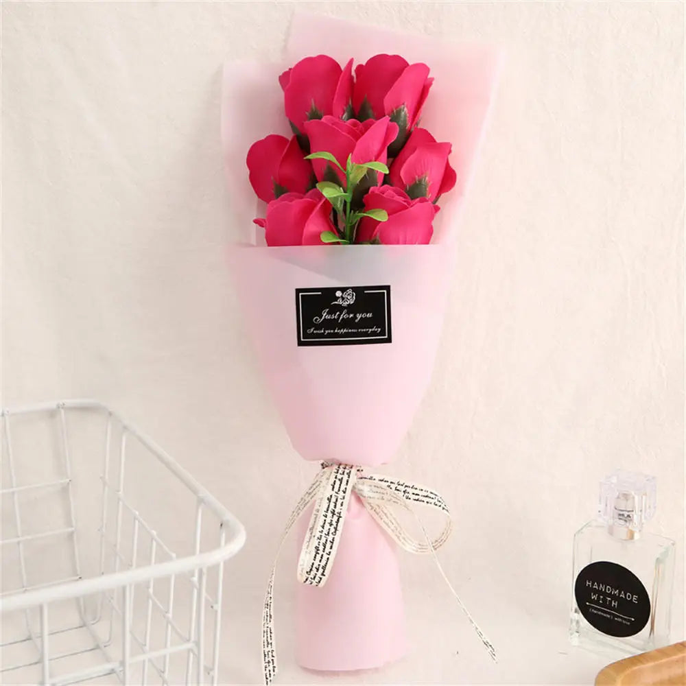 A pink vase holds a bouquet of vibrant pink roses with a black tag and twine bow.