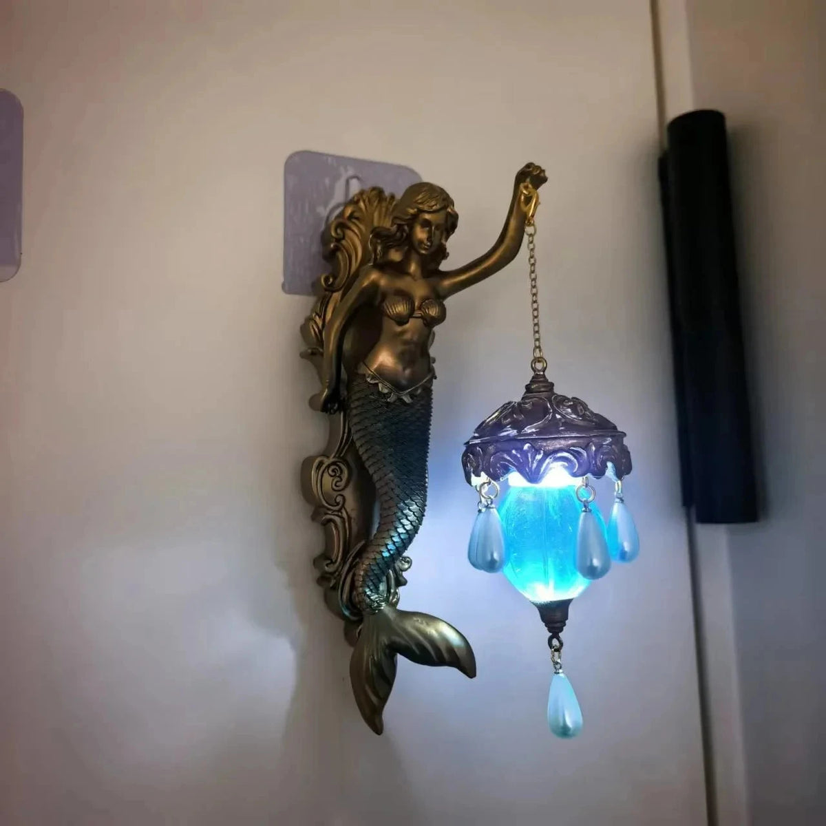 A bronze resin sculpture of a mermaid with a tail, mounted as a wall lamp.