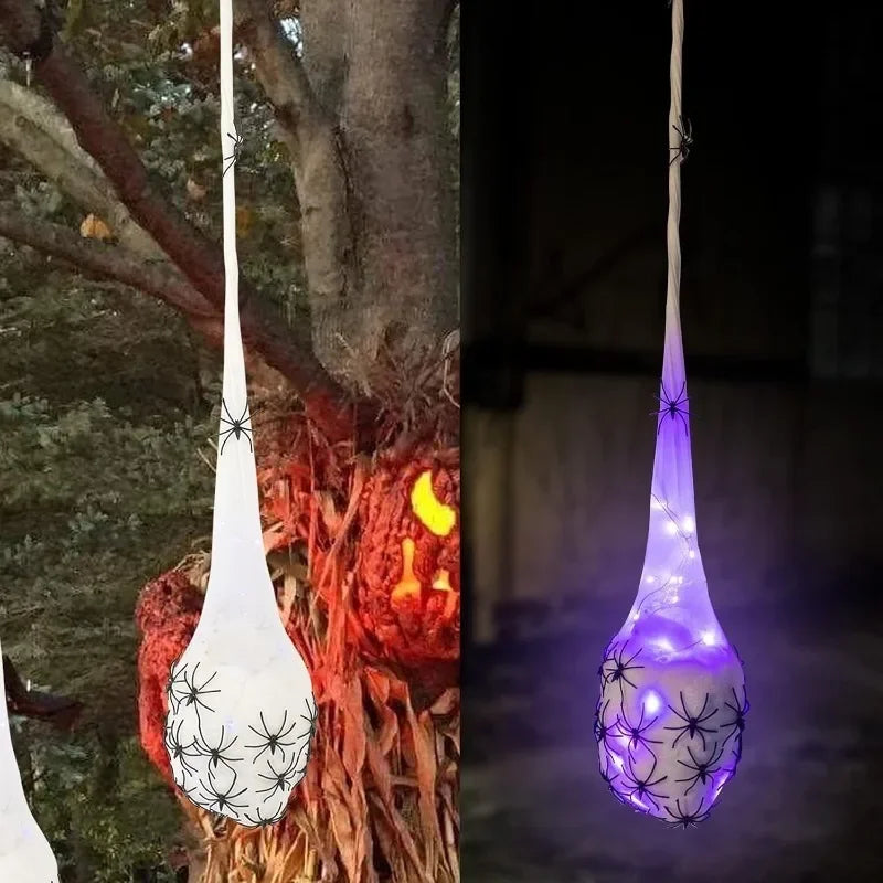 A glowing Halloween decoration featuring a white spider web and light-up eggs hanging from a tree branch.