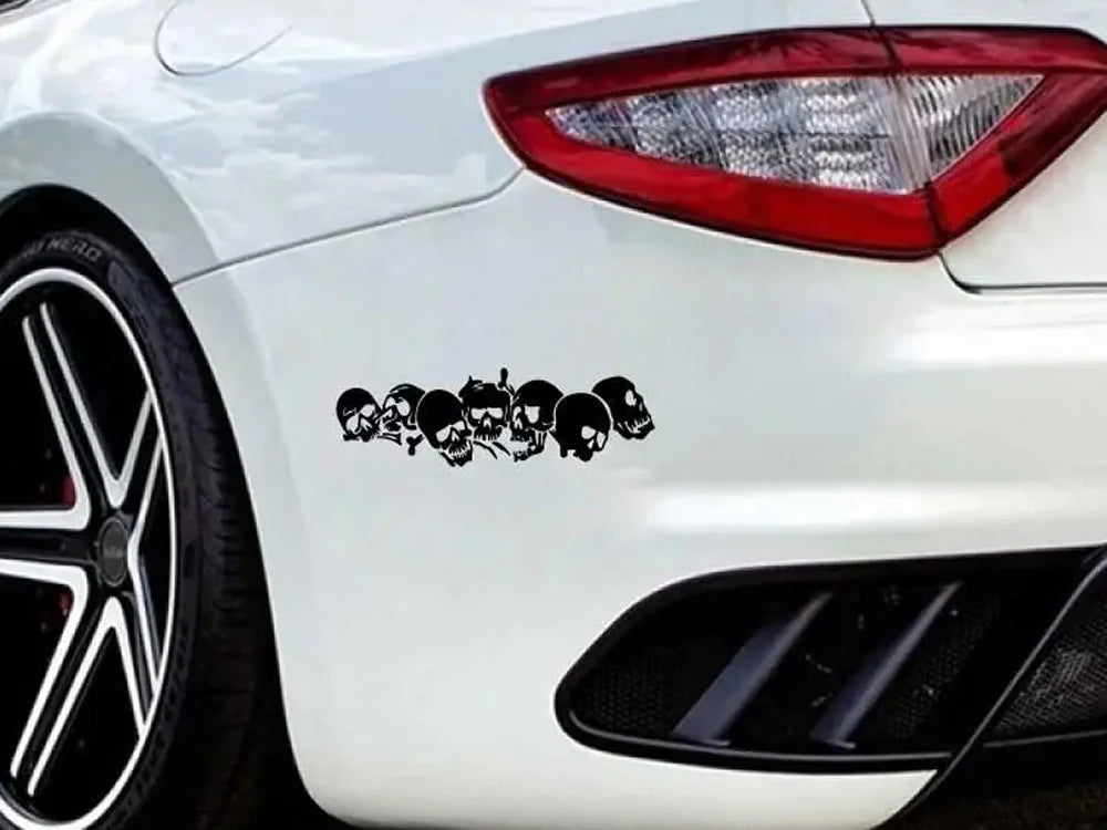 A close-up of a white car's rear section featuring a black decal of multiple skulls and skeletons on the body panel.