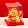 A yellow solar-powered waving lucky cat figurine inside a clear red display box.