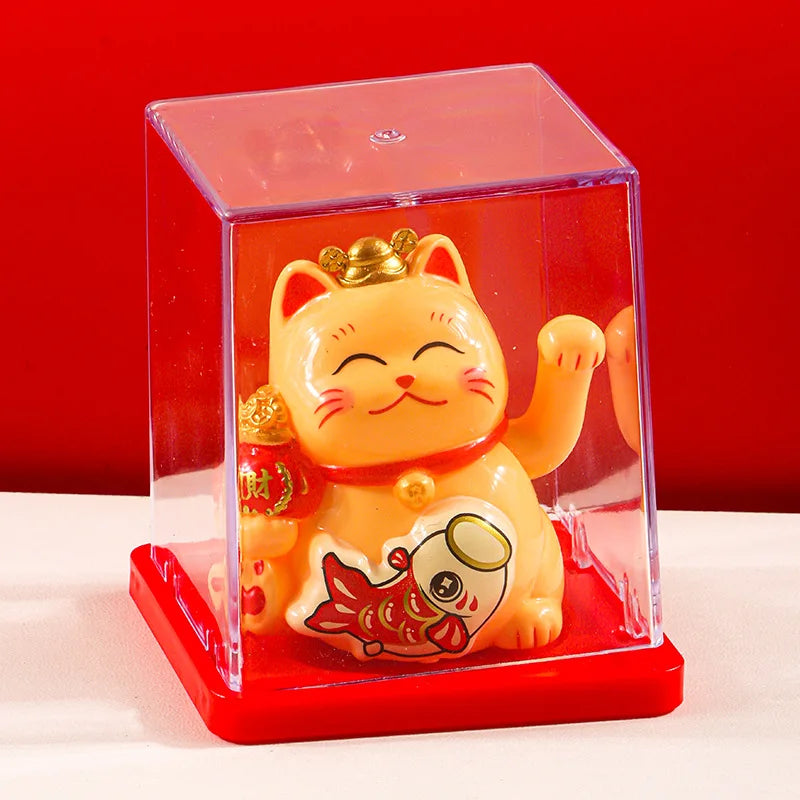 A yellow solar-powered waving lucky cat figurine inside a clear red display box.