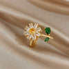 A gold cocktail ring featuring a flower design with clear and green gemstones on a satin background.