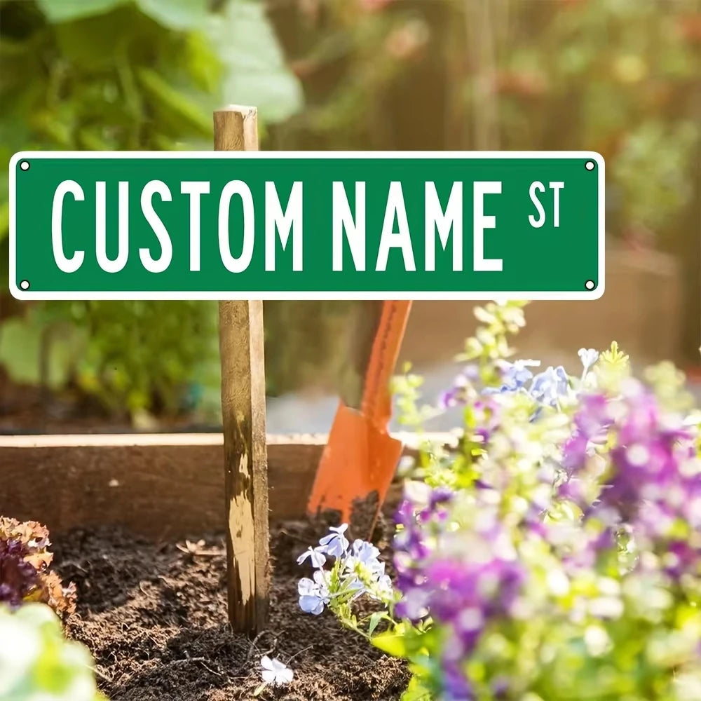 A wooden post holds a green sign with the text CUSTOM NAME ST in an outdoor garden setting.