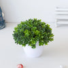 Un vibrant arbre bonsai artificiel vert dans un pot blanc, posé sur une surface blanche.