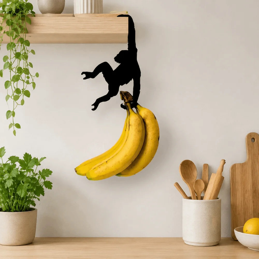 A black monkey-shaped storage hook with a banana design is mounted on a wooden shelf.