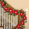 A festive red poinsettia garland with lights decorates a wooden staircase railing.
