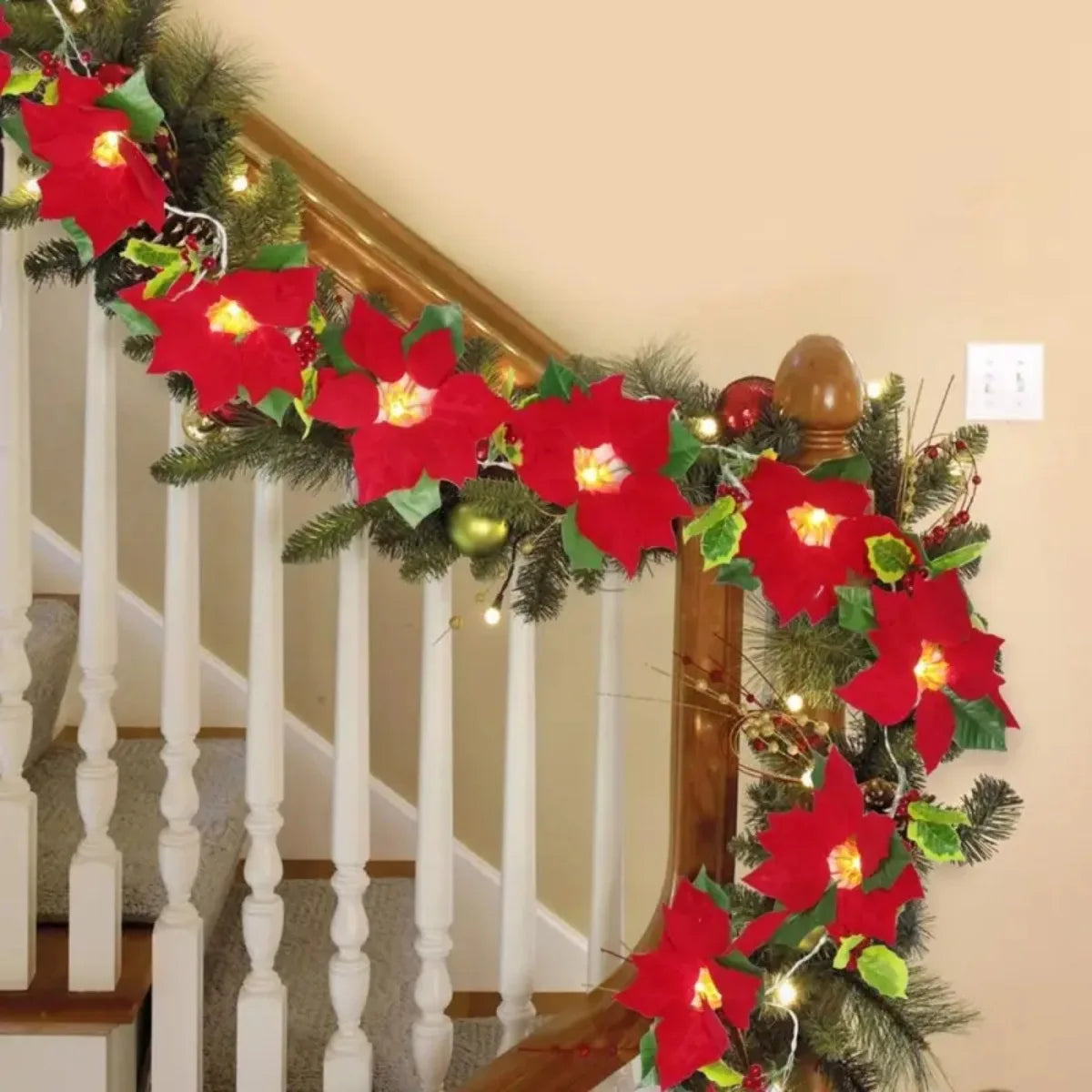 A festive red poinsettia garland with lights decorates a wooden staircase railing.