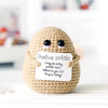 A handmade knitted plush potato doll with a positive message tag sitting on a white surface.