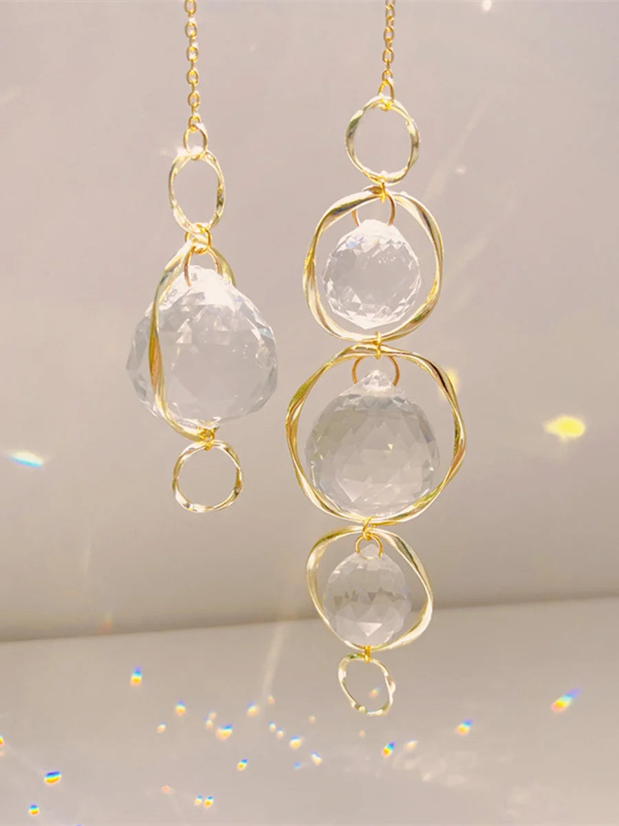 Une paire de pendentifs en cristal doré avec des pierres claires sphériques, suspendus par des boucles.